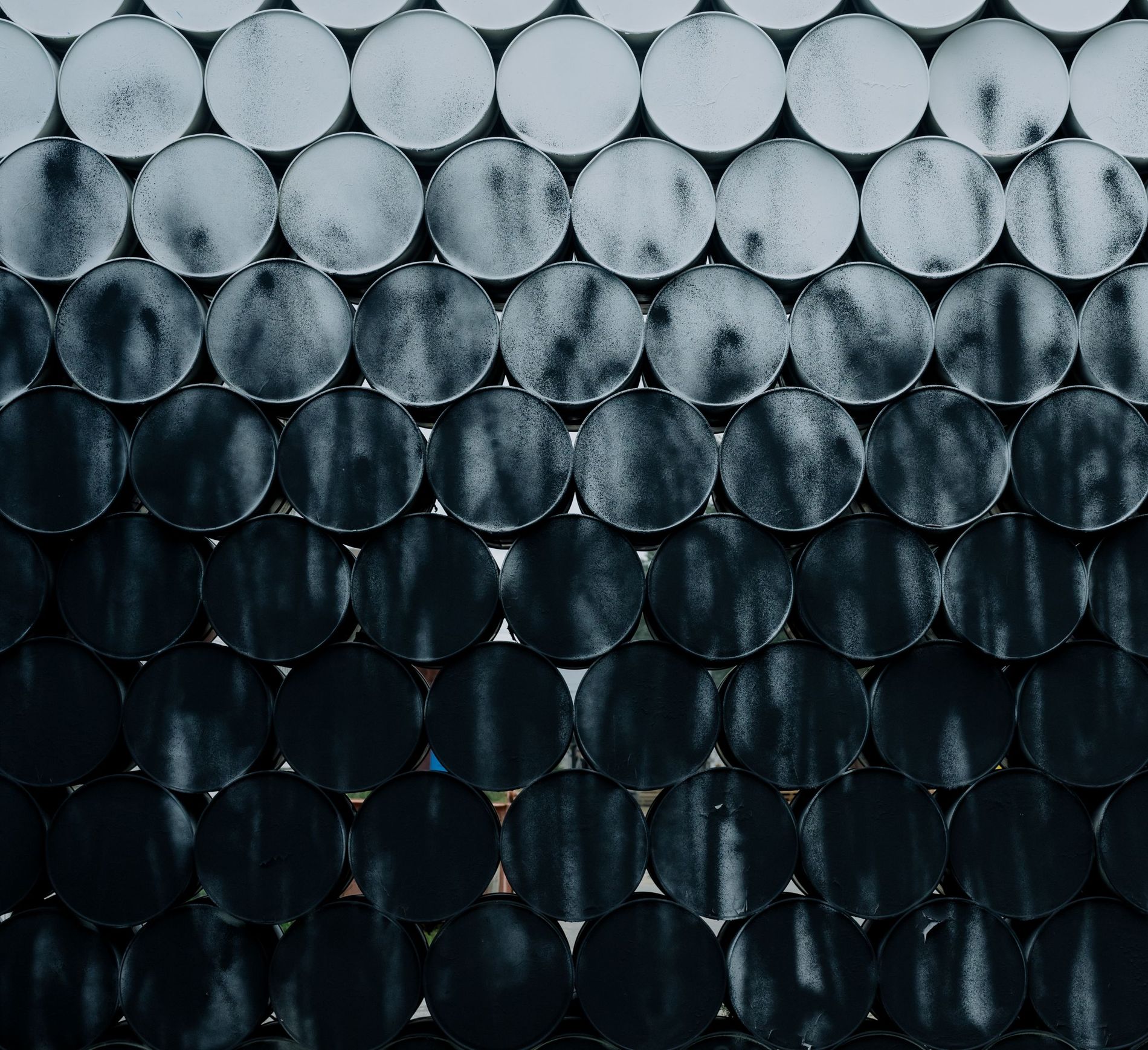A wall of stacked steel drums seen end-on, lit rows above falling away to shadow below
